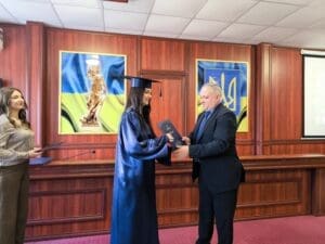 Професор Савчук Роман Михайлович вітає випускницю з отриманням диплома на тлі символіки України.